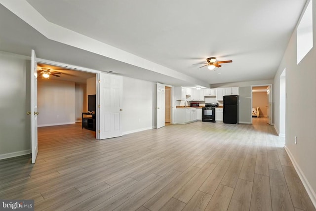 unfurnished living room with baseboards, ceiling fan, and light wood-type flooring