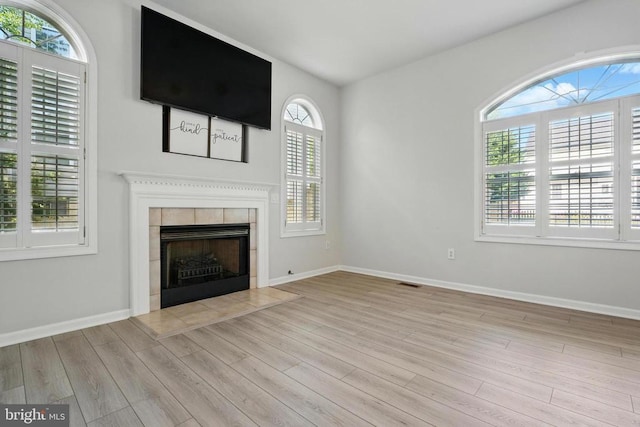 unfurnished living room with baseboards, visible vents, wood finished floors, and a tile fireplace