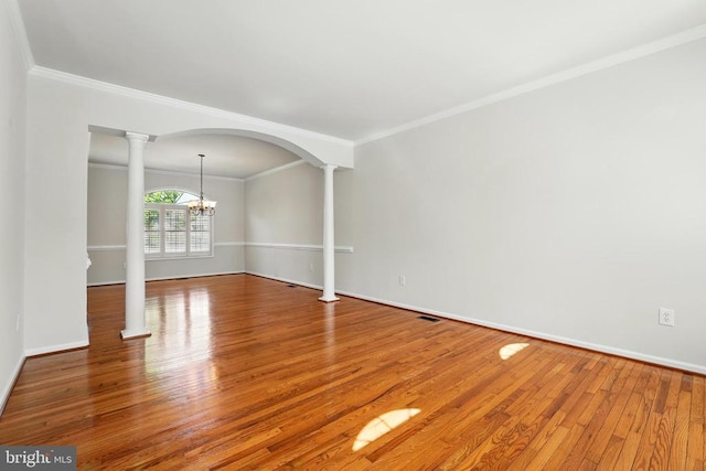empty room with wood finished floors, baseboards, a chandelier, ornamental molding, and ornate columns