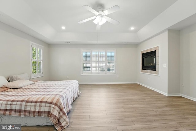 bedroom with light wood-type flooring, recessed lighting, baseboards, and a tray ceiling