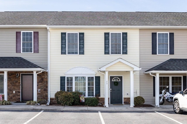 view of property with a shingled roof and uncovered parking