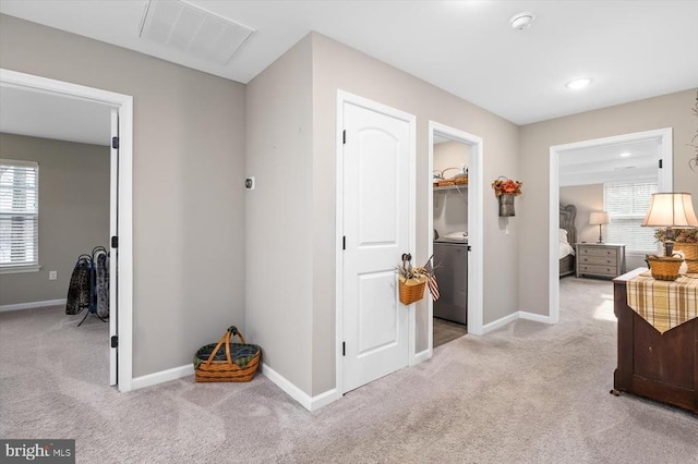 corridor with plenty of natural light, washer / clothes dryer, and light carpet