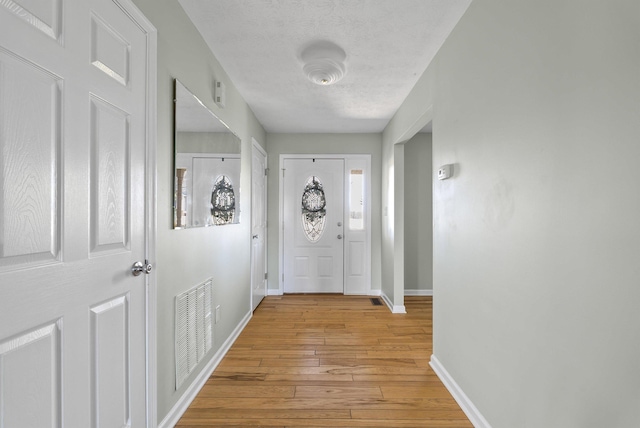 foyer featuring visible vents, baseboards, a textured ceiling, and light wood-style flooring