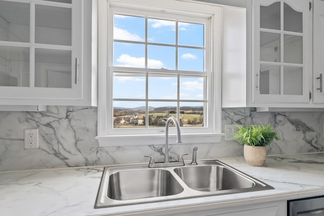 kitchen featuring tasteful backsplash, glass insert cabinets, light stone counters, white cabinets, and a sink