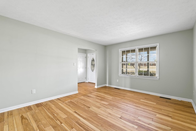 spare room with light wood finished floors, visible vents, a textured ceiling, and baseboards