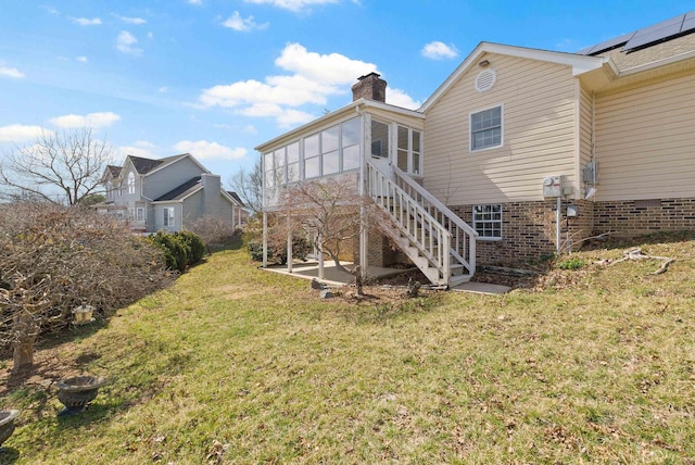 rear view of property featuring a chimney, a yard, solar panels, stairs, and a patio area