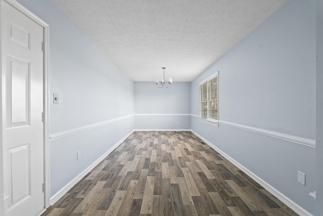 unfurnished dining area featuring a notable chandelier, dark wood-type flooring, a textured ceiling, and baseboards