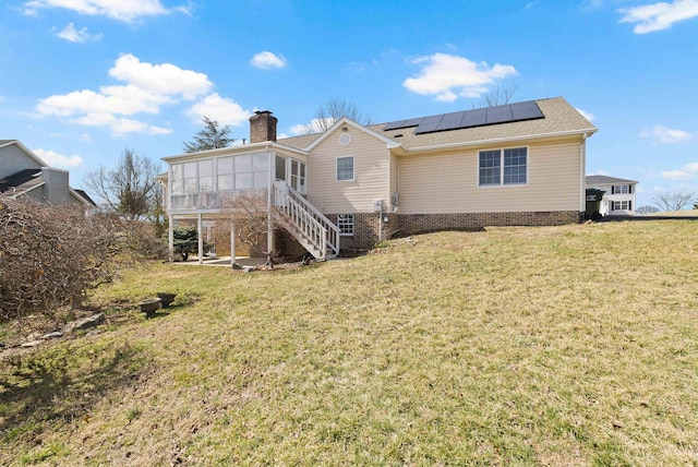 back of house with a yard, roof mounted solar panels, a sunroom, and a chimney