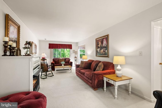 living room featuring baseboards, a warm lit fireplace, and light colored carpet