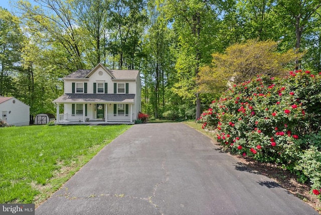 colonial home featuring a porch, a shed, a front yard, an outdoor structure, and driveway