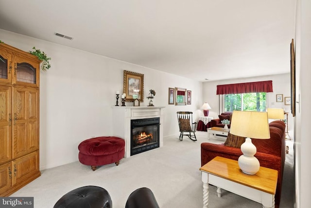 living area featuring visible vents, light carpet, and a glass covered fireplace