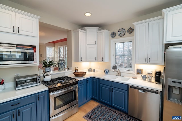 kitchen featuring white cabinetry, sink, blue cabinetry, and appliances with stainless steel finishes