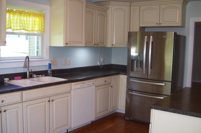kitchen featuring a sink, dark countertops, white dishwasher, cream cabinets, and stainless steel fridge