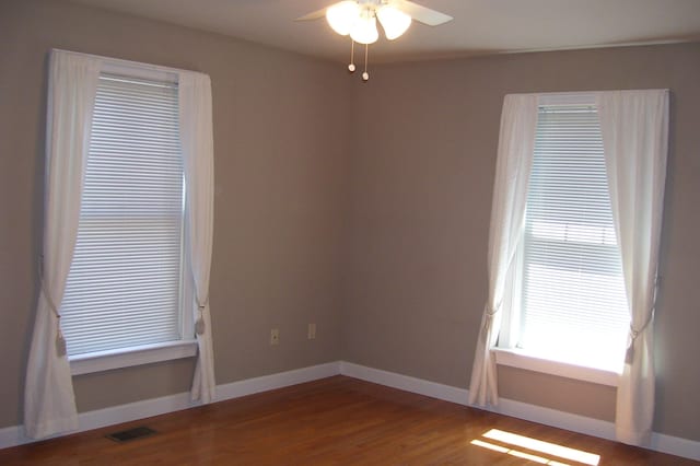 unfurnished room with wood finished floors, visible vents, ceiling fan, and baseboards