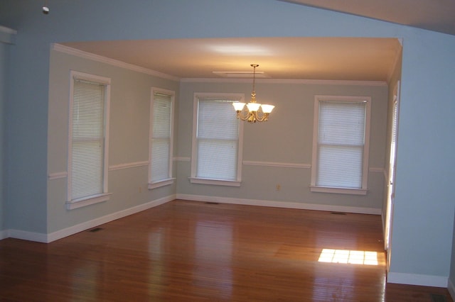 empty room with ornamental molding, wood finished floors, a chandelier, and baseboards