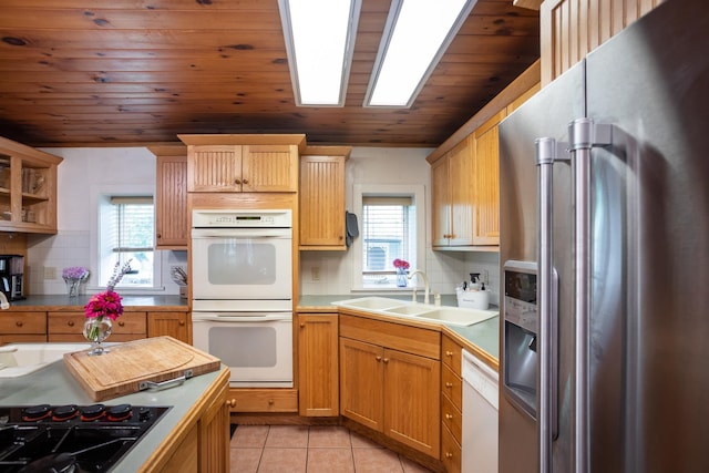 kitchen featuring white appliances, a skylight, light tile patterned flooring, plenty of natural light, and a sink