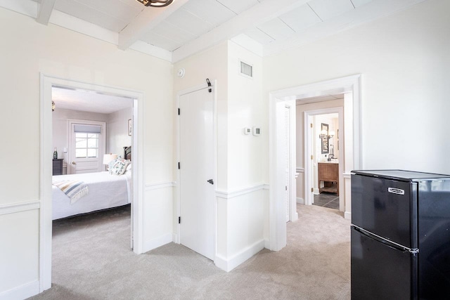 hallway with beam ceiling, light colored carpet, visible vents, and baseboards