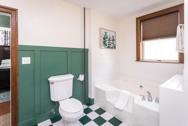 bathroom with a wainscoted wall, a garden tub, a decorative wall, toilet, and tile patterned floors