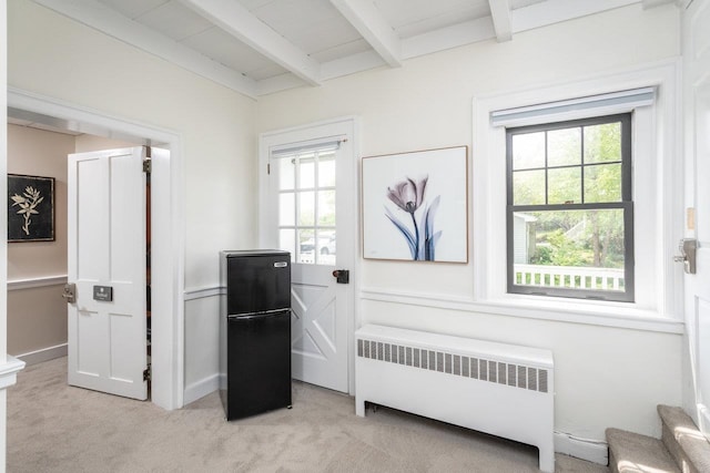 bedroom featuring beamed ceiling, multiple windows, light colored carpet, and radiator heating unit