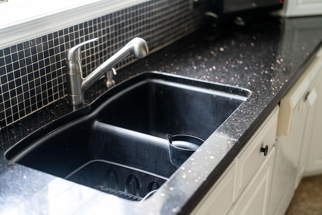 room details with dark stone counters, sink, and white cabinets