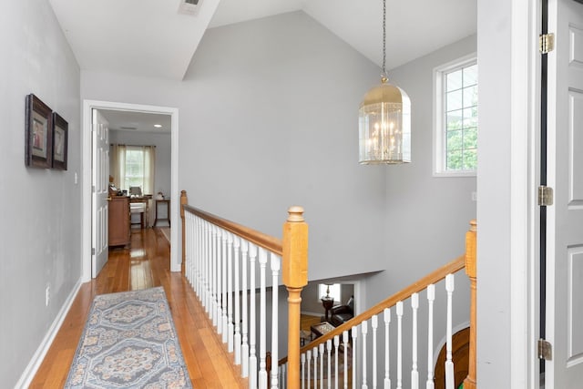 hallway with vaulted ceiling, an inviting chandelier, and light hardwood / wood-style flooring