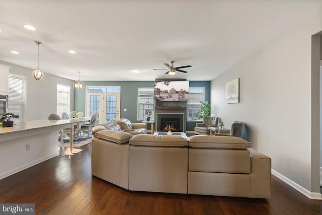 living area featuring baseboards, dark wood finished floors, a ceiling fan, a lit fireplace, and recessed lighting