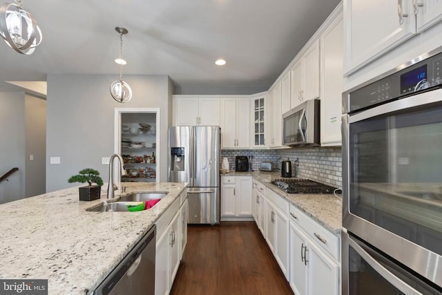 kitchen featuring appliances with stainless steel finishes, white cabinets, a sink, and decorative light fixtures