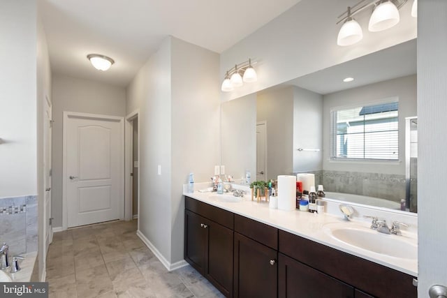 full bathroom with double vanity, a sink, a bath, and baseboards