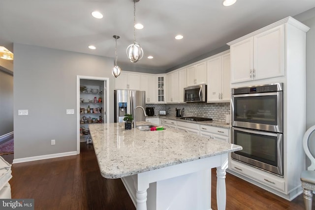 kitchen featuring pendant lighting, a center island with sink, stainless steel appliances, glass insert cabinets, and a sink