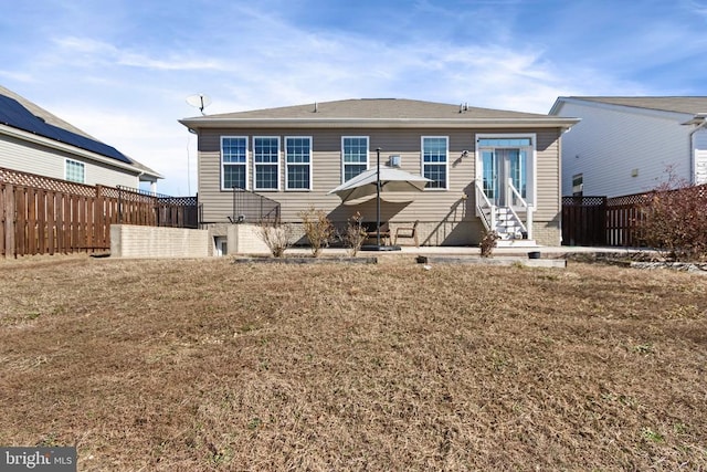 rear view of house featuring entry steps, fence, and a lawn