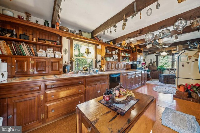 kitchen with a kitchen island, butcher block countertops, beamed ceiling, black dishwasher, and sink