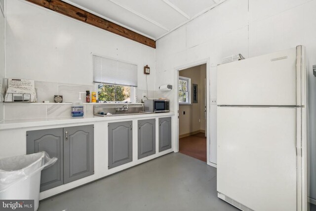 kitchen with beam ceiling, gray cabinets, sink, and white fridge