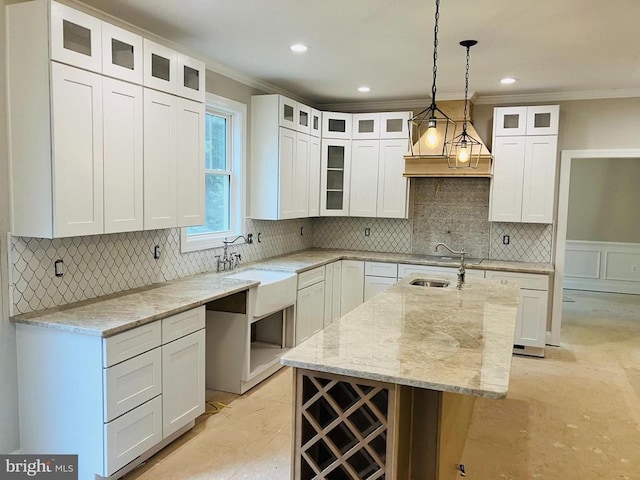 kitchen featuring white cabinets, an island with sink, glass insert cabinets, pendant lighting, and a sink