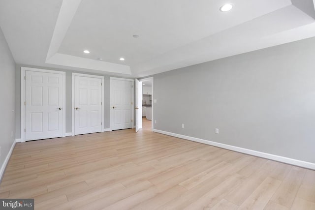 unfurnished bedroom with recessed lighting, baseboards, a raised ceiling, and light wood-type flooring