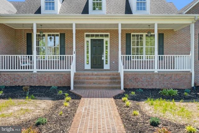property entrance with a porch, a shingled roof, and brick siding