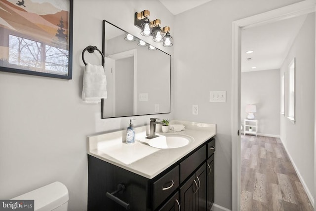 bathroom featuring baseboards, toilet, wood finished floors, and vanity