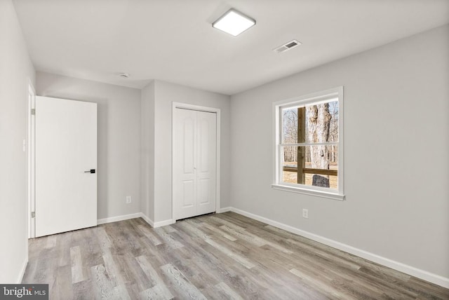 unfurnished bedroom featuring visible vents, baseboards, a closet, and wood finished floors