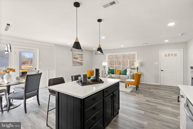 kitchen with visible vents, light wood-type flooring, light countertops, a kitchen bar, and dark cabinets