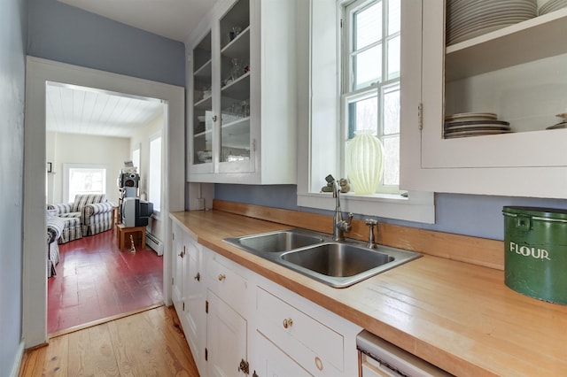 kitchen with sink, wooden counters, white cabinetry, a baseboard heating unit, and light wood-type flooring