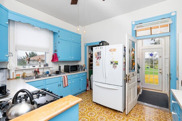 kitchen with sink, blue cabinetry, ceiling fan, and white refrigerator