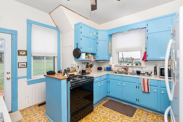 kitchen with black gas range oven, sink, ceiling fan, blue cabinets, and white fridge