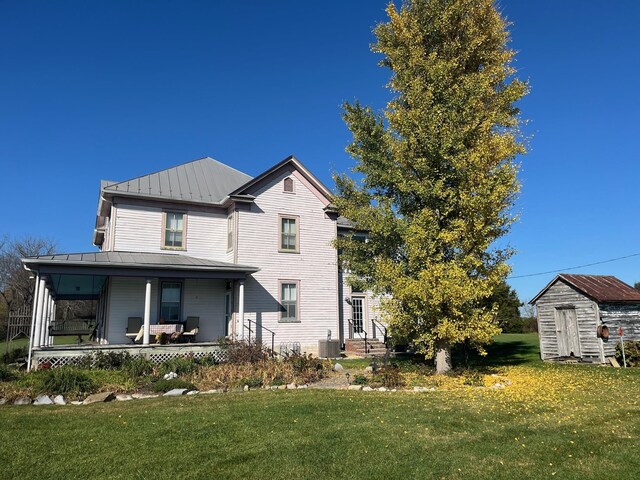 rear view of property with a porch, a storage shed, a yard, and central AC unit