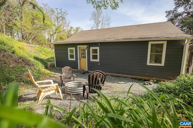 rear view of property featuring a shingled roof and an outdoor fire pit