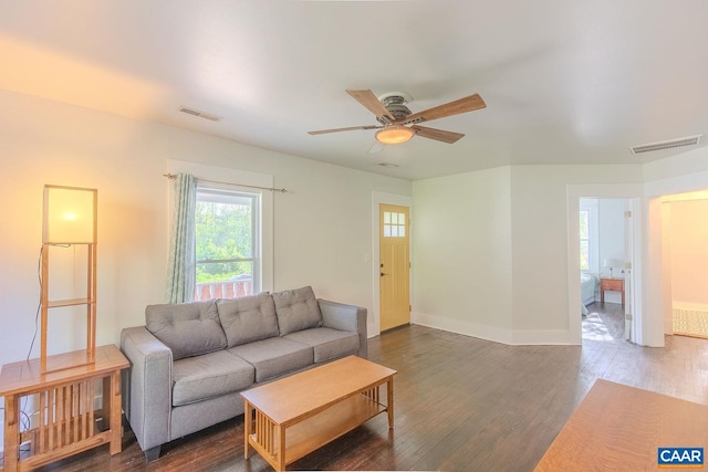 living room featuring visible vents, a ceiling fan, baseboards, and dark wood-type flooring