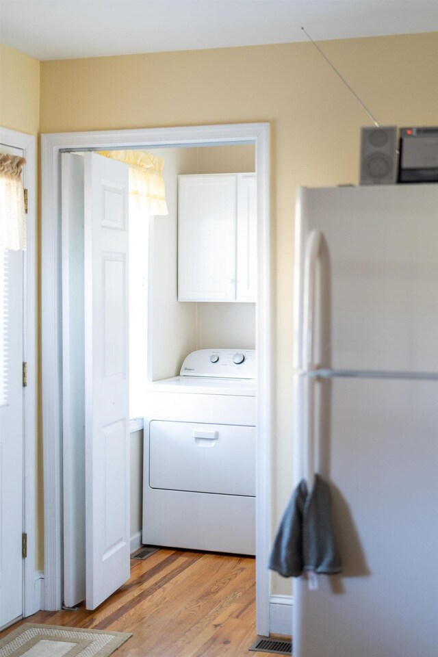 clothes washing area with cabinets, washer / dryer, and light hardwood / wood-style floors