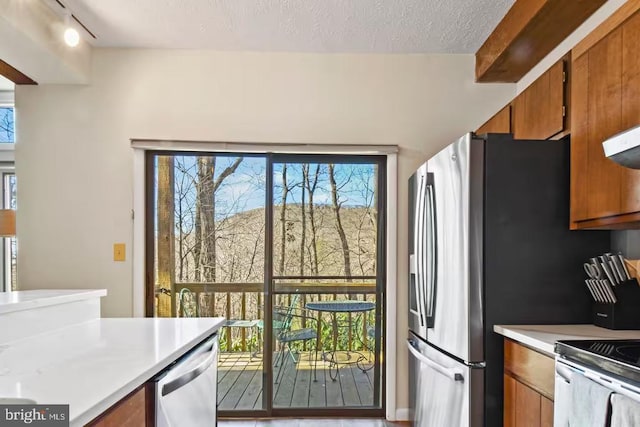 kitchen with stainless steel fridge, brown cabinetry, dishwasher, light countertops, and a textured ceiling