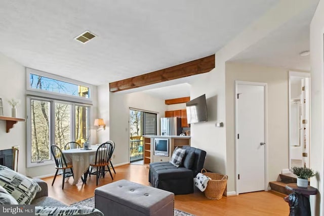 living area featuring light wood-type flooring, visible vents, a fireplace, and beamed ceiling