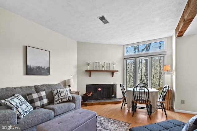 living area with a glass covered fireplace, visible vents, light wood-style flooring, and baseboards