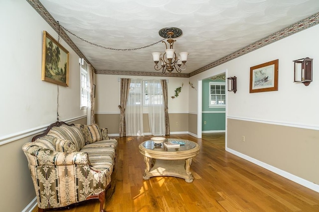 living room with wood-type flooring, crown molding, and an inviting chandelier