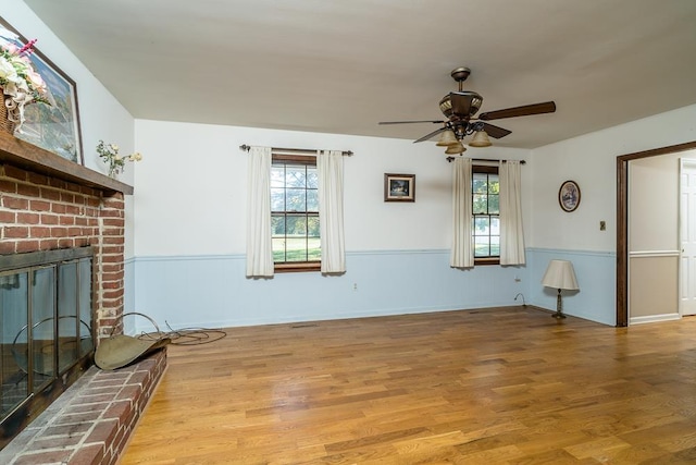 unfurnished living room featuring a brick fireplace, ceiling fan, and light wood-type flooring